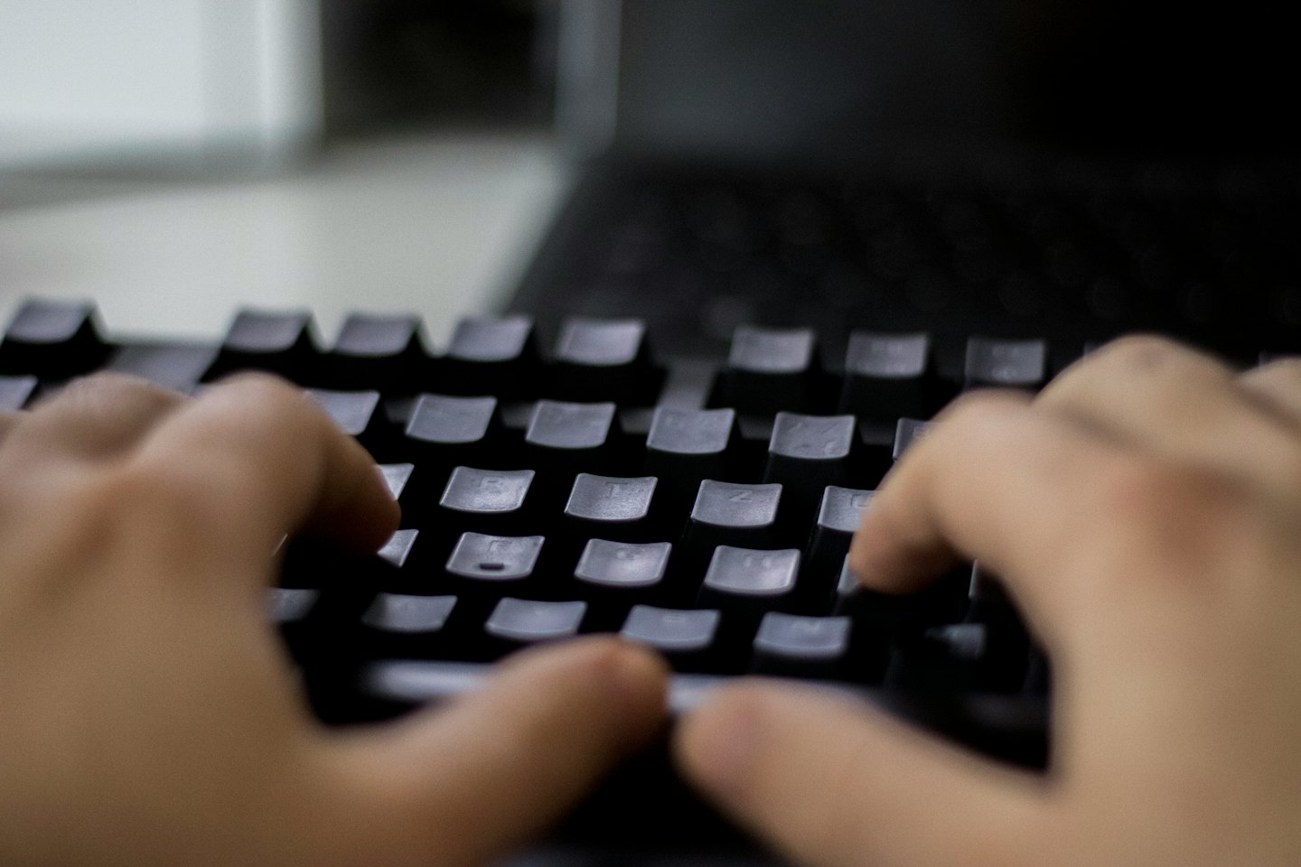 Hands typing on a black computer keyboard in an office.