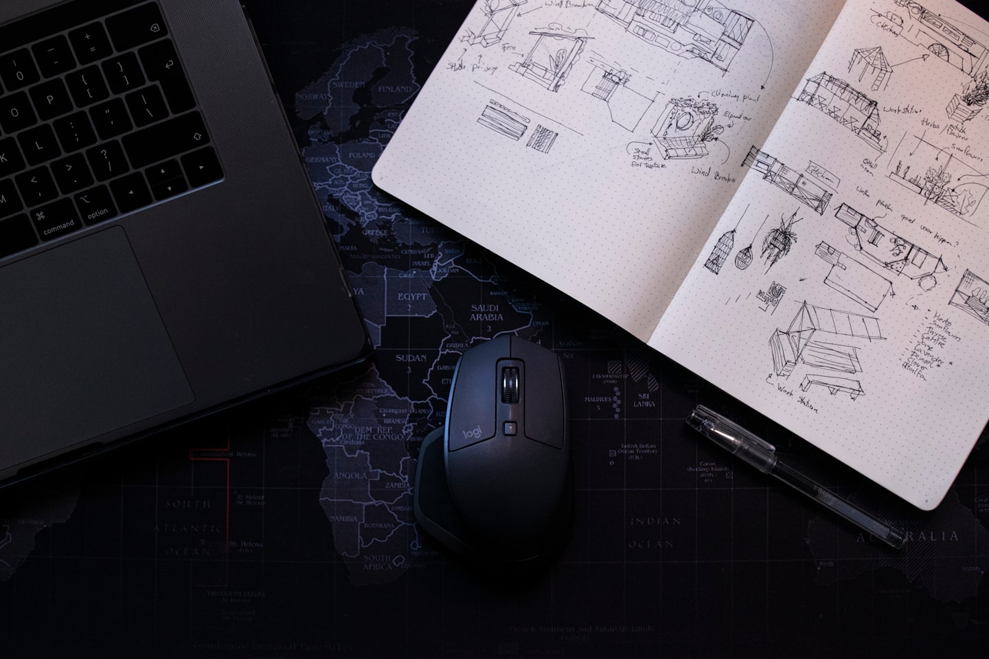Desk with laptop, notebook sketches, and mouse on world map.