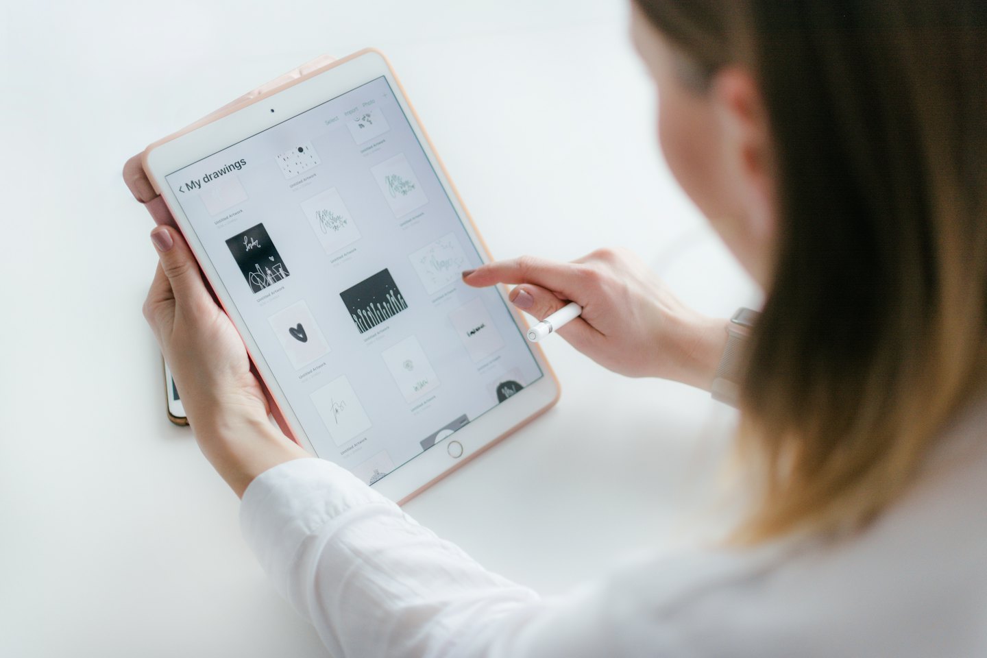 Hands using a rose gold tablet to browse digital art.